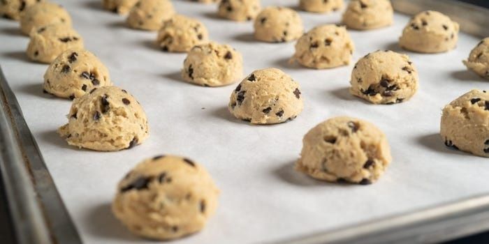 Klickar av kakdeg med chokladbitar på en bakplåt